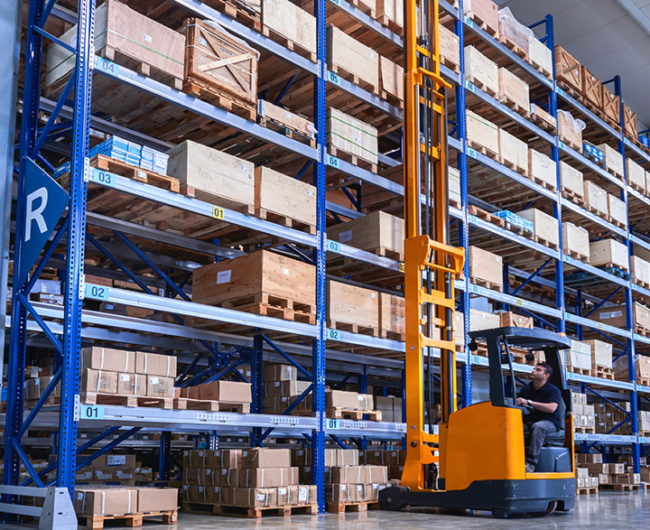 An orange forklift working next to a blue shelving system